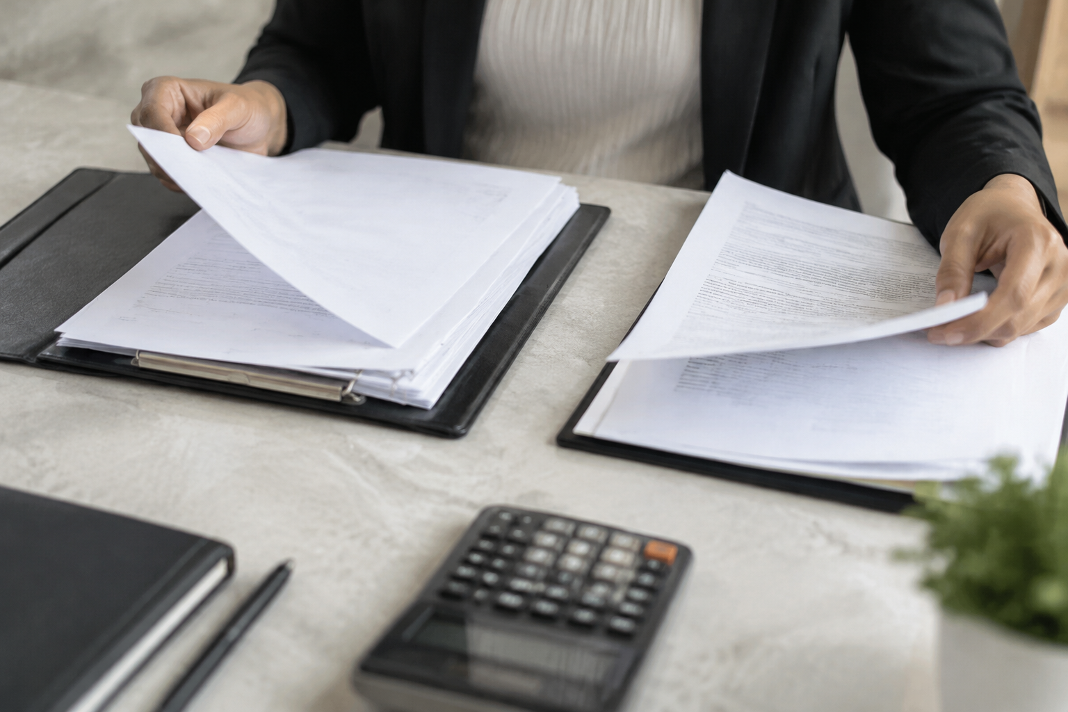 Pessoa compara documentos financeiros ao lado de uma calculadora.